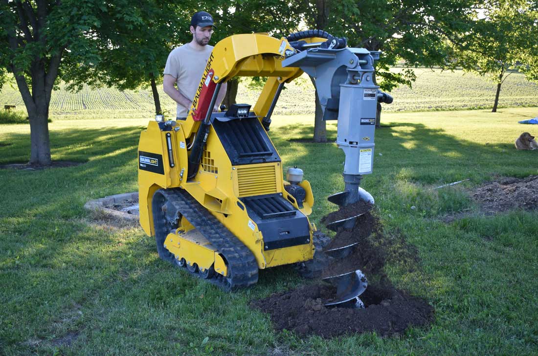 Mini track loader with pengo auger bit in drilling action