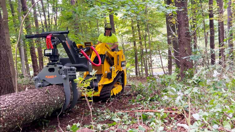 Mini-chargeuse sur chenilles TRL630D avec pince à grumes traînant un arbre abattu