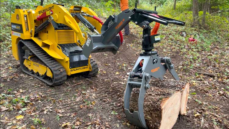 Mini-chargeuse sur chenilles TRL630D avec pince à grumes soulevant une grume